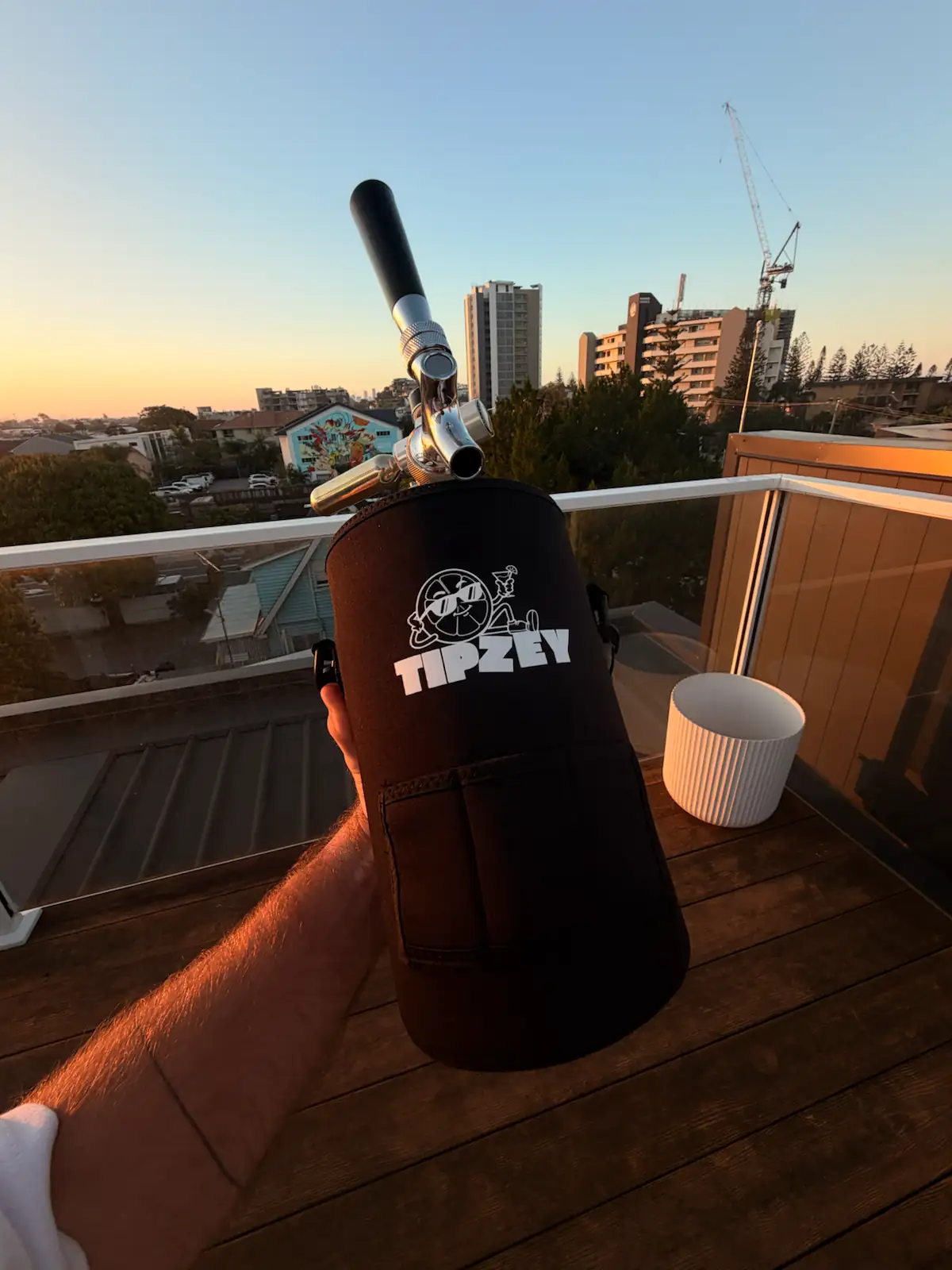 Holding a black Tipzey mini keg on a balcony at sunset